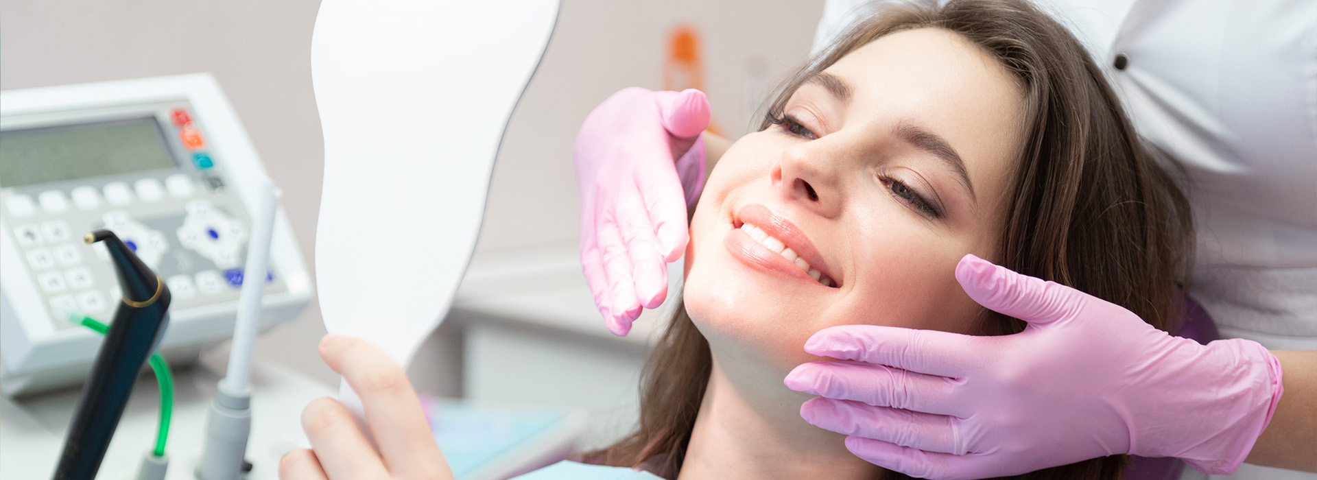 A person receiving dental care with a hygienist performing treatment, using a mirror to inspect their teeth while sitting in a dentist s chair.