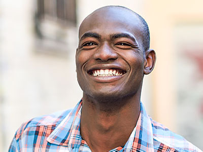 A smiling man with short hair wearing a plaid shirt, standing outdoors during daylight.